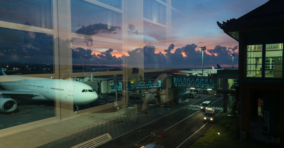 1:05 for transfer at Manchester airport - Through glass modern aircraft parked near airbridge in contemporary airport against picturesque dusk sky