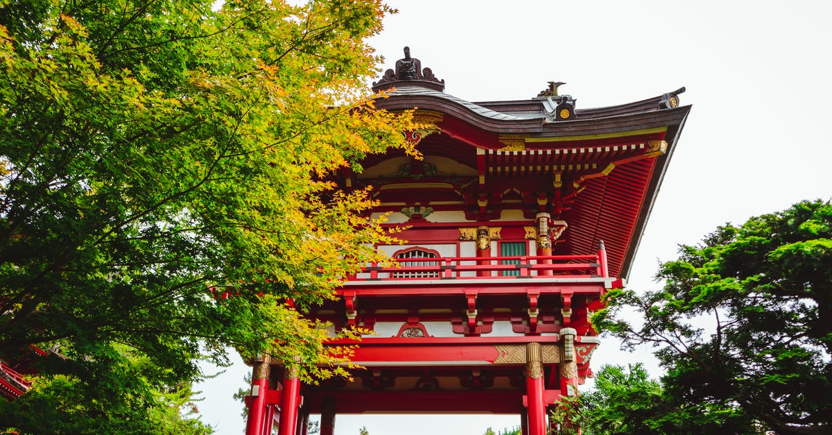 17 year old US Citizen traveling to Canada - Low angle exterior of traditional aged red Asian temple surrounded by lush green trees in Japanese Tea Garden located in San Francisco on sunny day