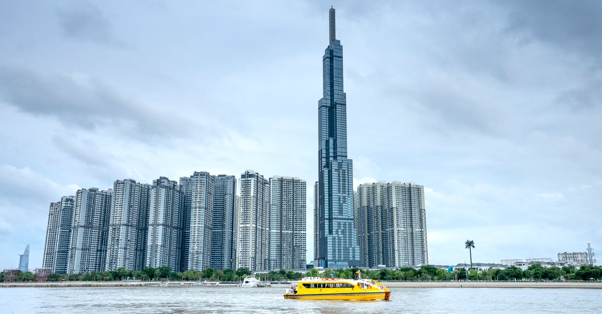 1 day Hạ Long Bay tours from Hanoi, Vietnam - Picturesque scenery of Ho Chi Minh City in Vietnam with skyscrapers and Landmark 81 building on coast with trees near water with ferry under cloudy sky in summer day