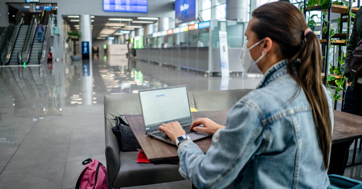 1 Hour 10 Minute Connection in New Istanbul Airport - Side view of concentrated female freelancer in protective mask typing on netbook while sitting at table in modern airport terminal