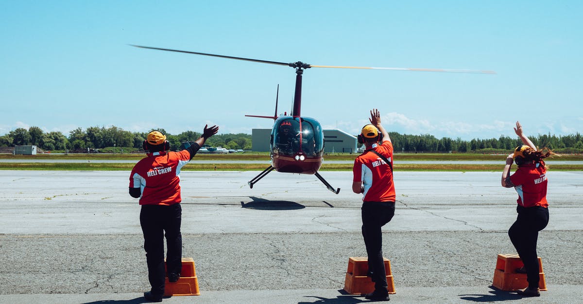 1 hour 50 min layover at PEK (Beijing International Airport) - Back view of anonymous ground crews in uniforms and headsets meeting passenger helicopter on airfield after flight against cloudless blue sky