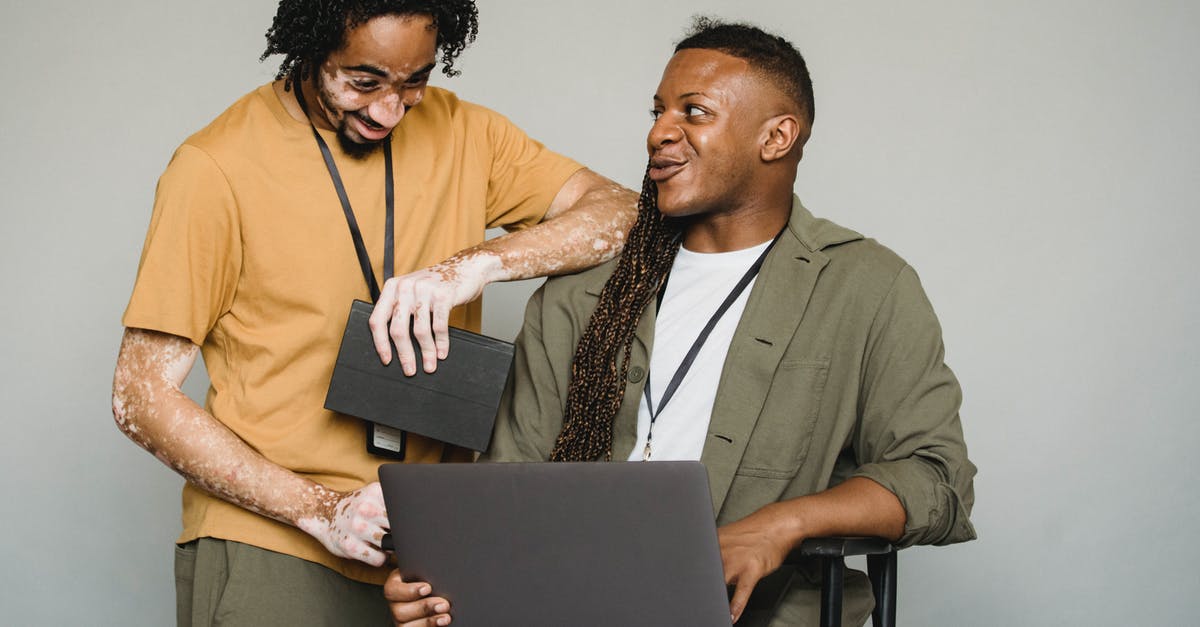 2 passports,2 different names, not OK dual citizenship - Happy African American androgynous person with Afro braids and computer looking at black colleague with vitiligo and notebook while working on gray background