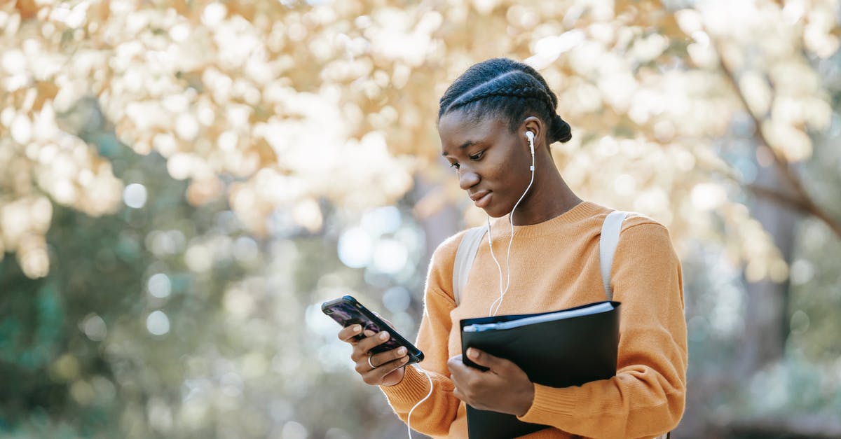 50-minute connection in Helsinki between Schengen and non-Schengen - enough time? - Positive young African American female student with earphones and folder using mobile phone in park