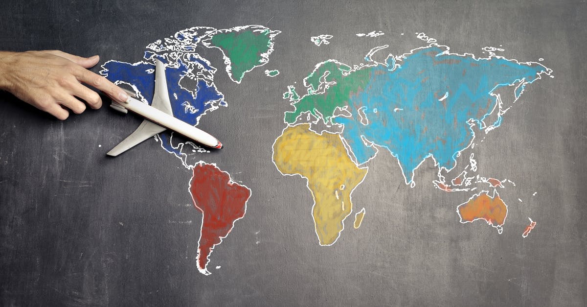 6 AM flight from Marseille to Paris - Top view of crop anonymous person holding toy airplane on colorful world map drawn on chalkboard