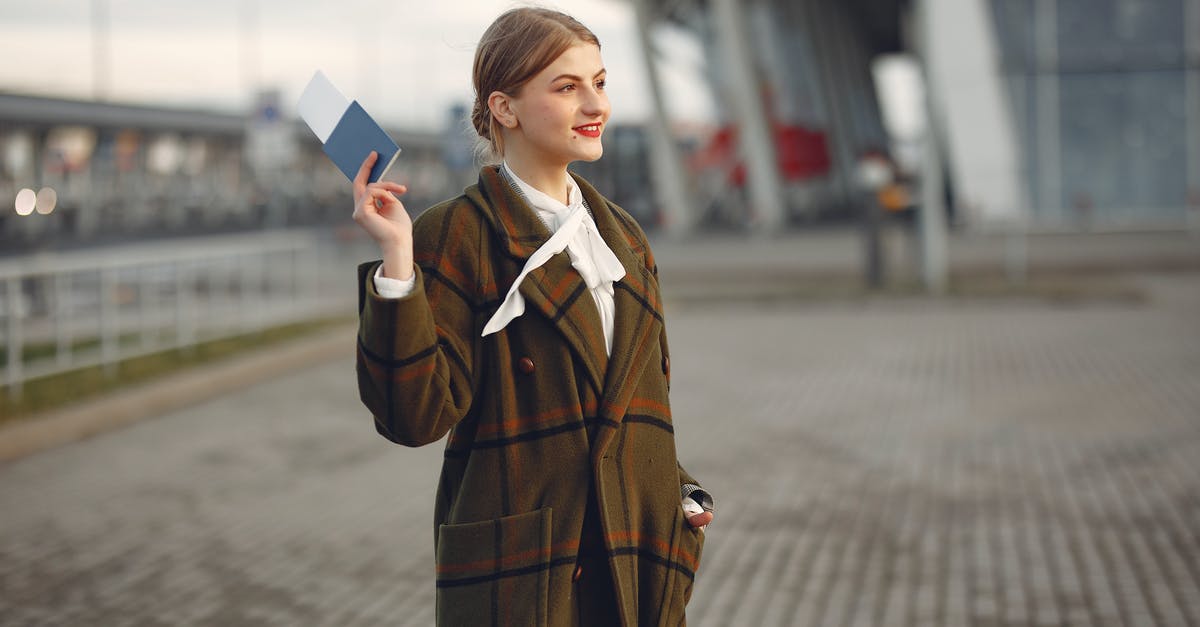 A Convention Travel Document (CTD) or Titre de Voyage [closed] - Cheerful female passenger wearing trendy plaid coat taking passport and ticket in raised hand while standing on pavement near modern building of airport outside and looking away with smile