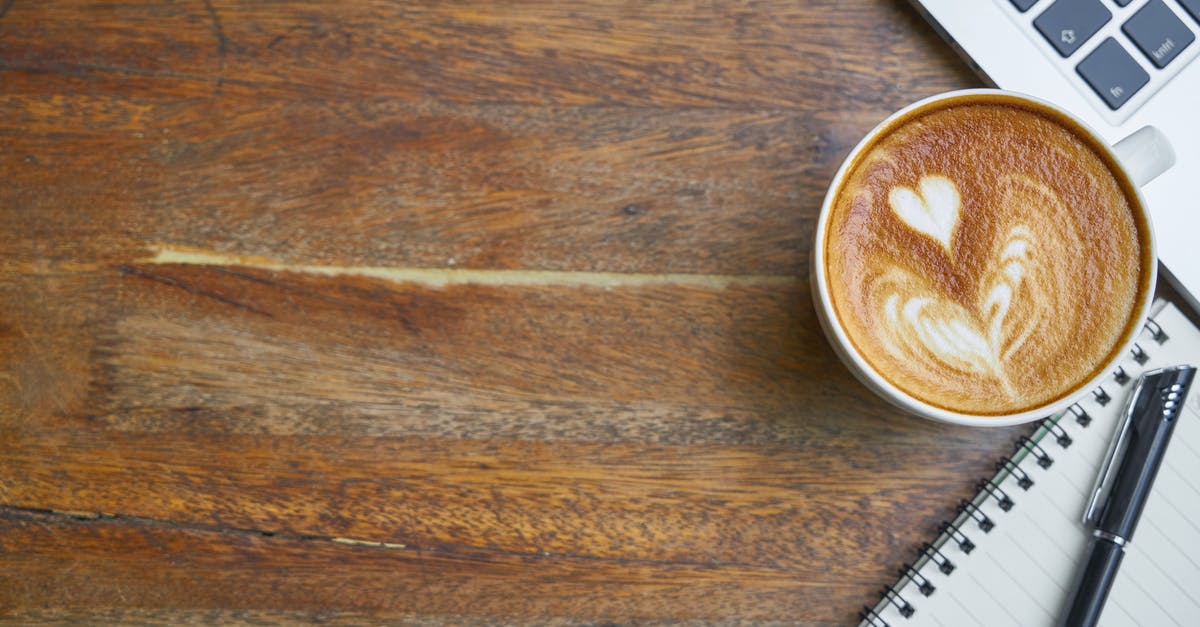 A normal desktop computer [closed] - Cup of fresh cappuccino near laptop keyboard and notebook