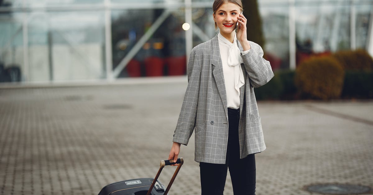 A phone setup for frequent international travel - Stylish businesswoman speaking on smartphone while standing with luggage near airport