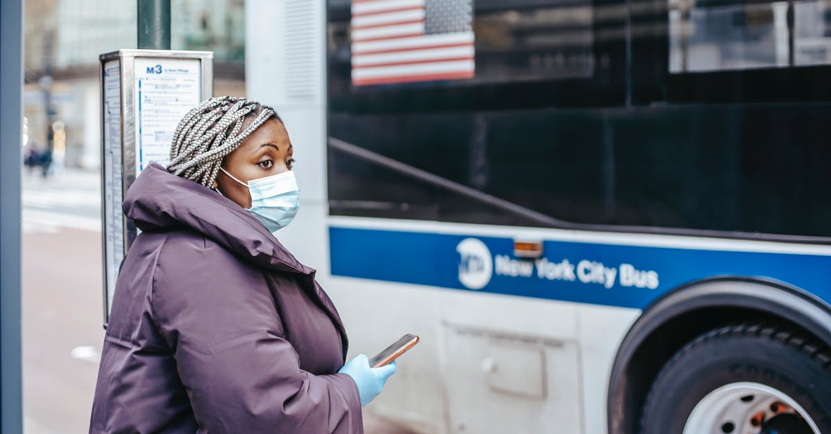 About travelling Canada to USA by Bus - Ethnic doctor with smartphone against urban bus