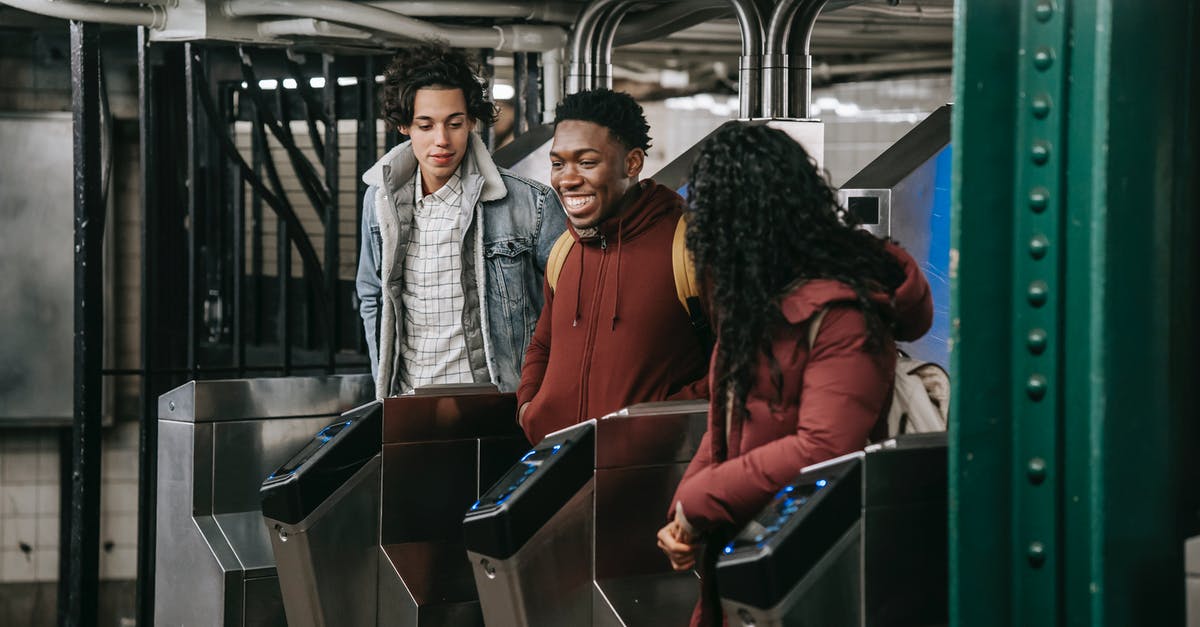 Accessing Group Fare Concessions - Positive multiethnic group of friends in warm clothes walking through automatic metal gates in subway platform while entering railway station