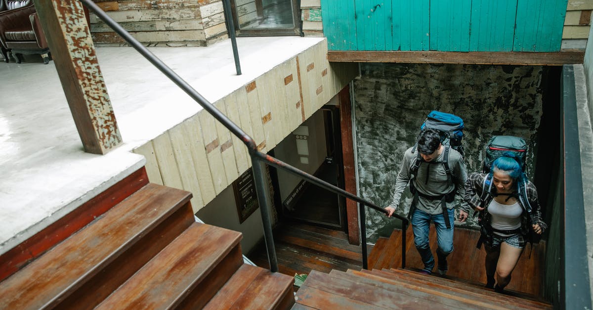 Accommodation at relative's during standard visit visa in UK - From above of anonymous man and woman in casual clothes and with backpacks walking upstairs in modern apartment