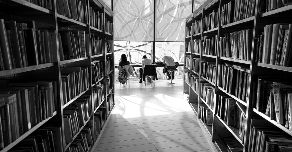 Accompanying my wife (who is student) as a visitor - Black and white back view of distant anonymous group of visitors studying at table in library with assorted books on bookshelves