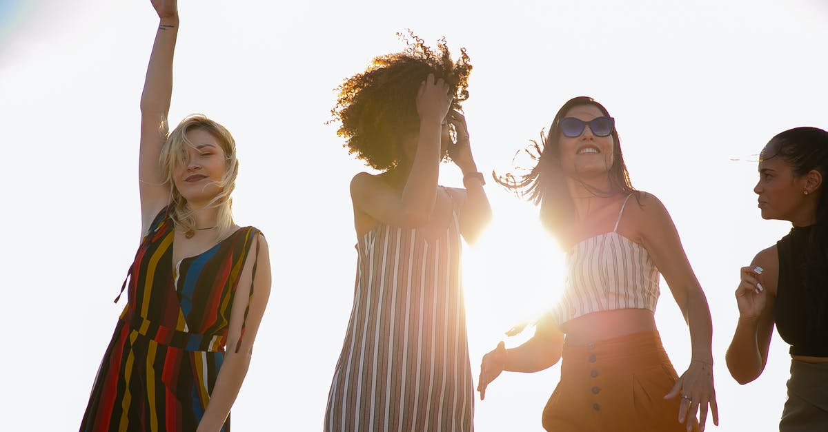 Activities in Montreal for a Bachelor party - From below of young content diverse ladies in trendy outfits smiling and dancing against cloudless sky during open air party on sunny day