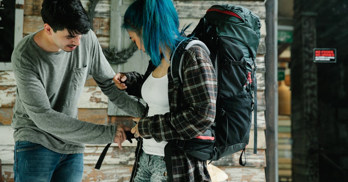 Actual enforcement of carry-on luggage weight [closed] - Side view of young multiracial couple of tourists in casual clothes carrying backpack while standing near wooden wall and preparing for travel