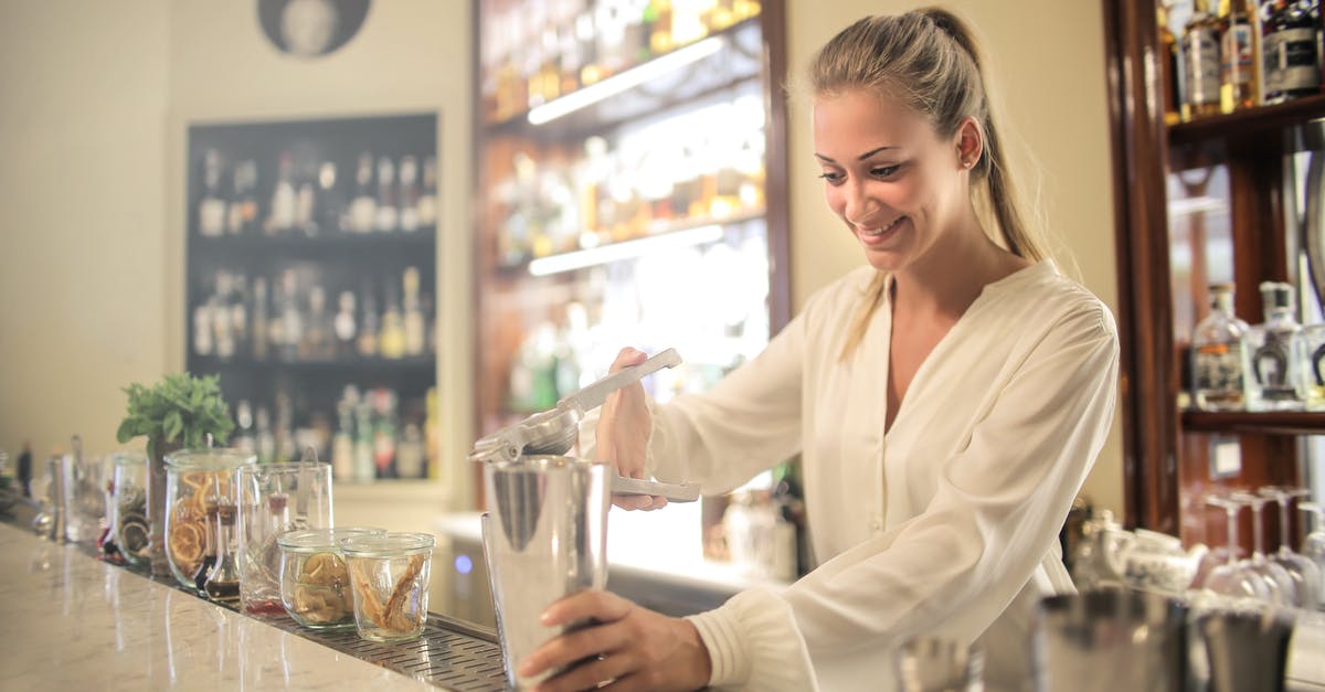 Add passenger for flights booked with Wizz Discount club - Smiling blonde in white blouse squeezing fresh juice into stainless shaker while preparing cocktail in bar