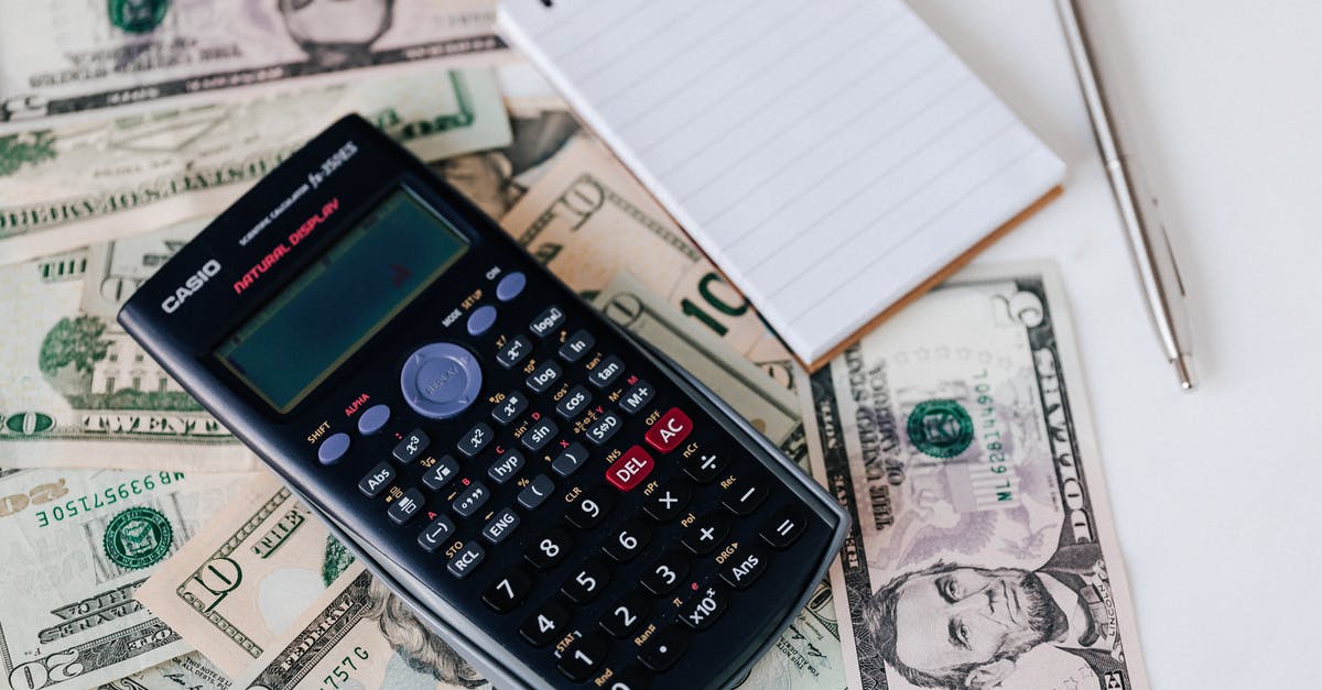 Additional luggage fee from US to Europe with a domestic connection - From above electronic calculator and notepad placed over United States dollar bills together with metallic pen for budget planning and calculation