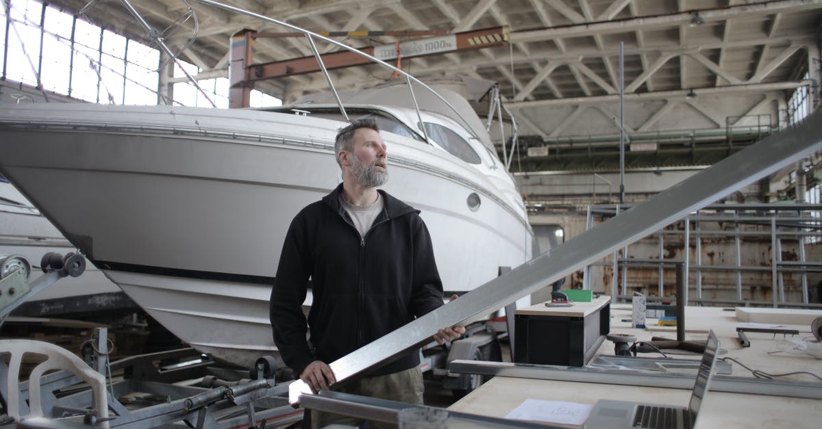 Affordable taxi service from BUF Airport to Niagara Falls on the Canadian side - Side view of adult bearded workman in casual clothes standing near workbench and controlling metal detail in garage with yachts