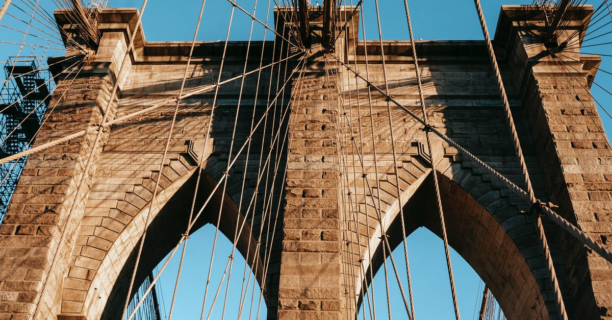 Affordable way to visit USA from UK? [closed] - Low angle of famous Brooklyn brick arches with ropes on top of bridge in metropolis