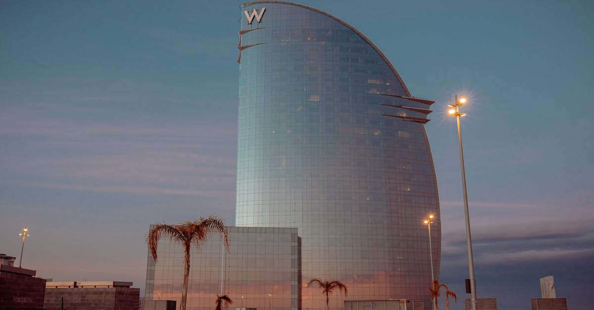 Air China number of bags Spain to Brazil - Contemporary building facade in form of sail against streetlights and anonymous people walking under sunset sky in Barcelona Spain