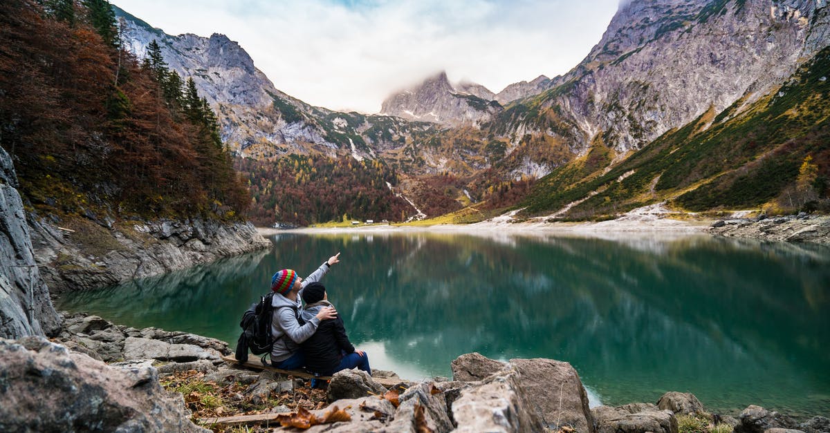 Air travel without known date - Couple Sitting on Rock Beside Lake