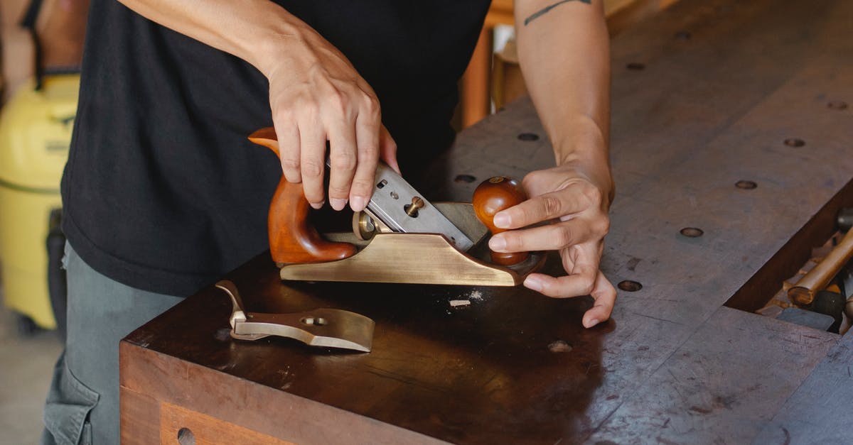 Airline Change of Equipment Code - Anonymous male carpenter with tattoo adjusting knife in planer for cutting wood during work in professional workshop on blurred background