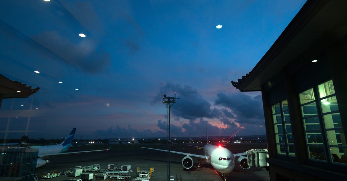 Airline responsibility during connection - Contemporary airplanes with red beacon parked on airfield near airport service vehicles and terminal at night