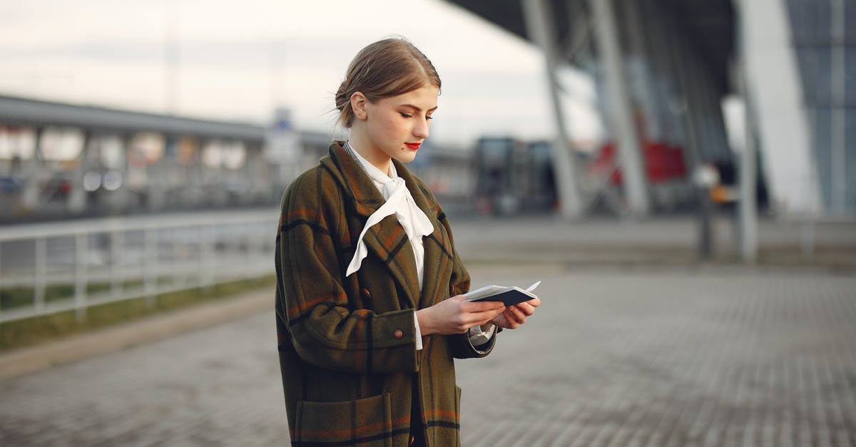 Airlines refusing check-in without return ticket - Attentive female passenger wearing trendy plaid coat and white blouse checking passport and ticket standing on pavement near modern building of airport outside