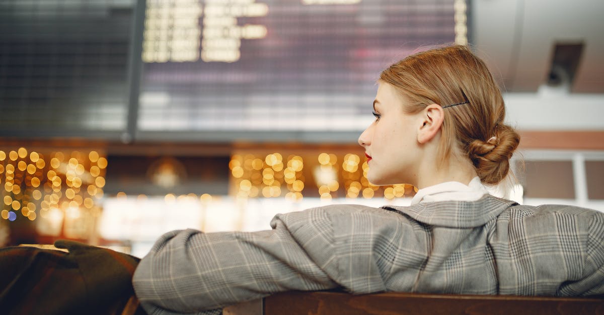 Airport Lounge in OR Tambo International Airport, Johannesburg - Pensive female designer in checkered jacket waiting for flight near departure board looking away in modern airport in evening