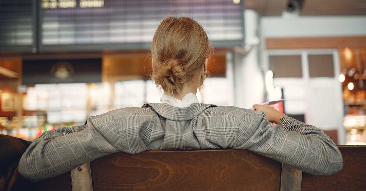 Airport Lounge in OR Tambo International Airport, Johannesburg - Back view of female employee in trendy jacket waiting for train departure and leaning on backs of wooden seats in train station