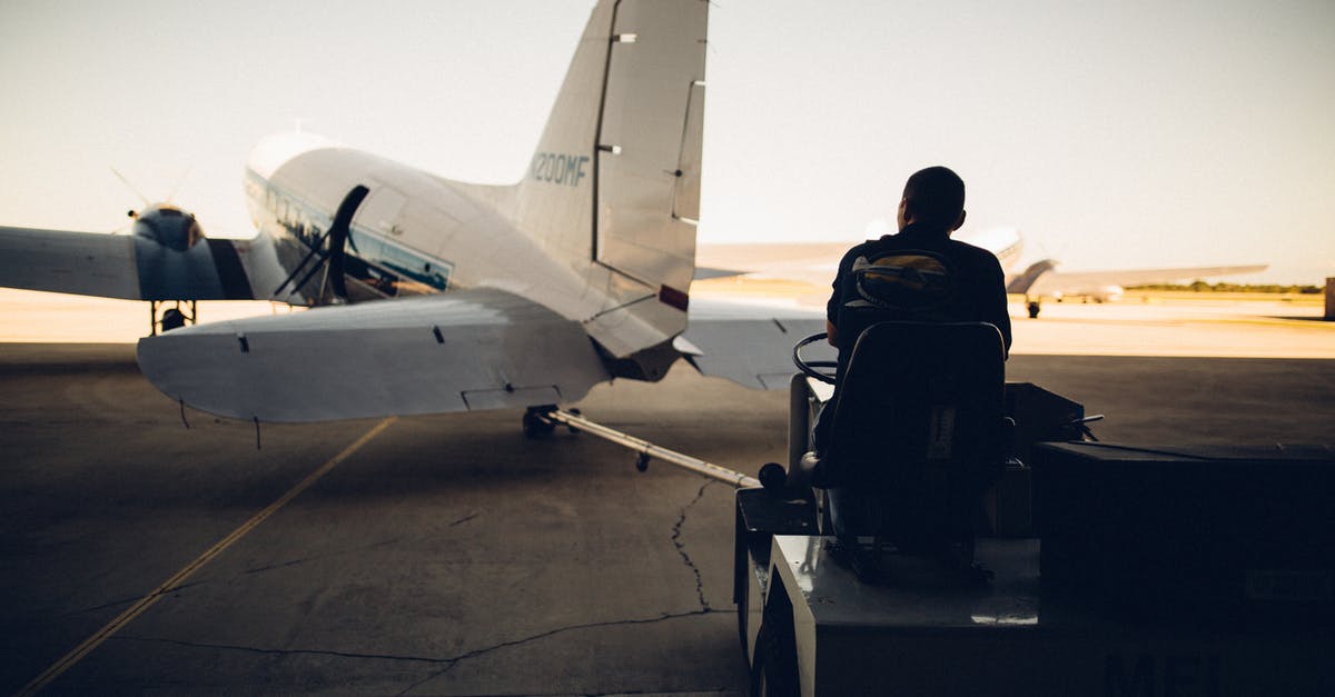 Airport security checkpoint controlling carry-on luggage amount? - Silhouette of worker driving baggage carrier on paved airfield with airplane before flight