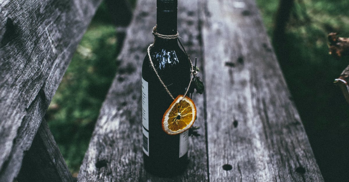 Alcohol as necessary medicine when visiting dry countries? - From above of glass bottle of wine with dried orange placed on old wooden bench in nature in daytime