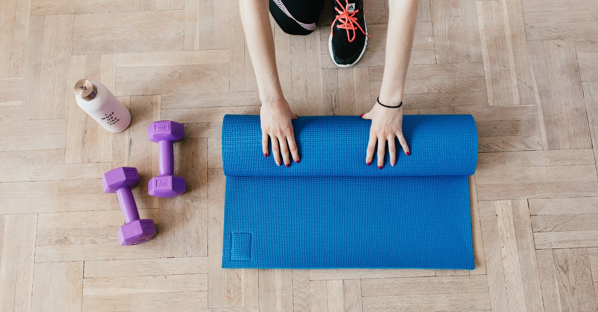 Alitalia hand baggage allowance in practice - Top view of anonymous female athlete in black leggings and sneakers unfolding blue mat for exercising on floor near dumbbells and water bottle in modern fitness center