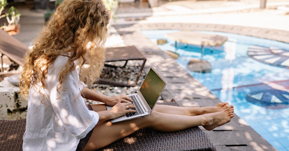 Allergic online resources for traveling - From above side view of unrecognizable barefoot female traveler with curly hair typing on netbook while resting on sunbed near swimming pool on sunny day