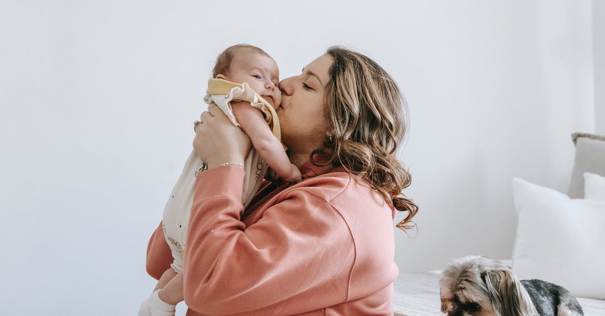 Am I able to carry on a small Swiss army knife? - Side view of happy woman kiss cute little baby while in bright room with puppy sitting on bed and