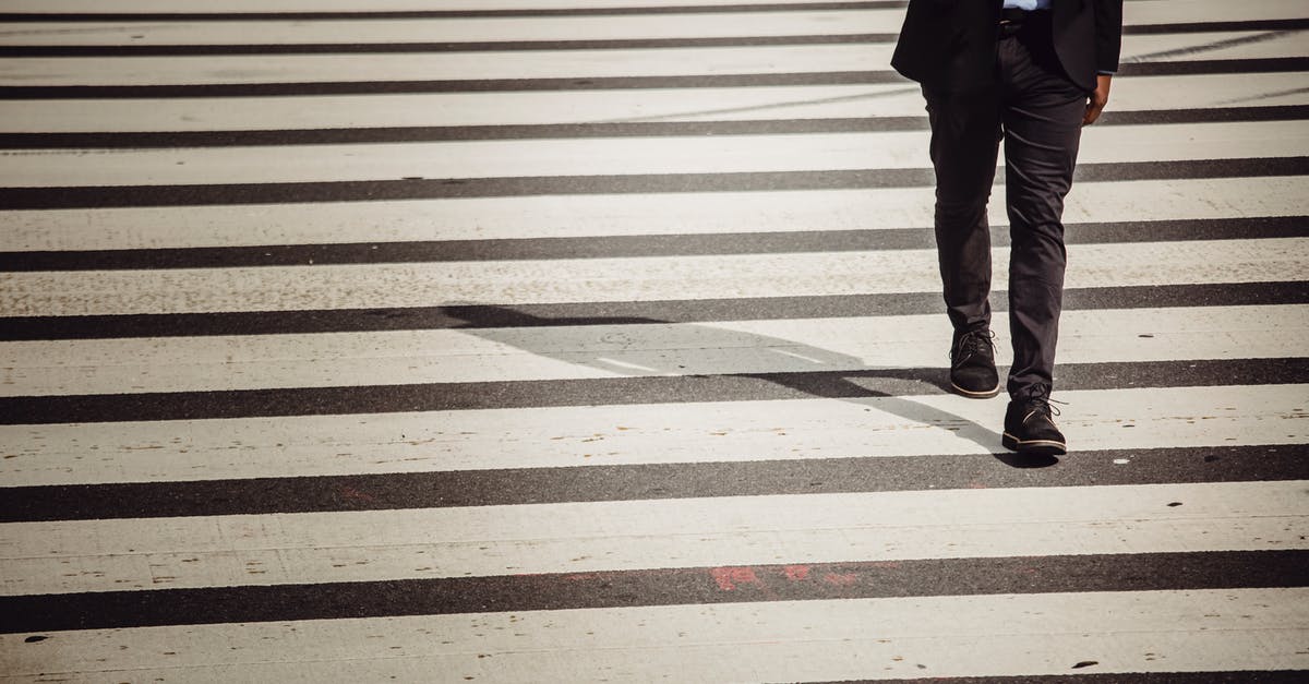 American citizen crossing from UK to France - Faceless businessman with smartphone walking on crosswalk in sunlight