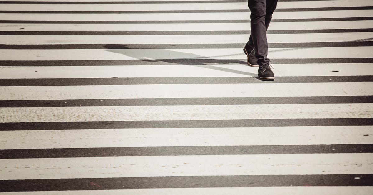 American citizen crossing from UK to France - Crop anonymous black person in black trousers and shoes walking on zebra crossing in sunlight