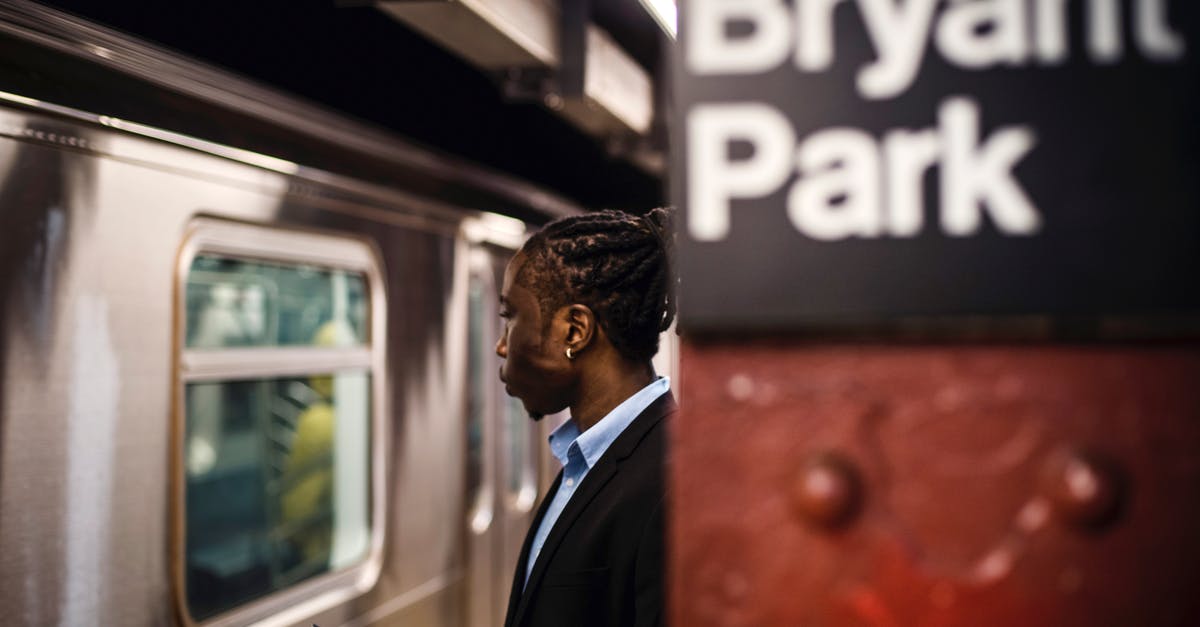 American Transit Visa for a Colombian - Side view of smart African American male with cellphone in hand waiting for arriving subway train to stop