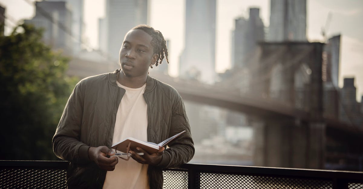 American with expired student visa traveling in Schengen zone - Young pensive African American male in casual clothes with open diary in hands leaning on balcony railing and looking away against blurred Brooklyn Bridge in summertime