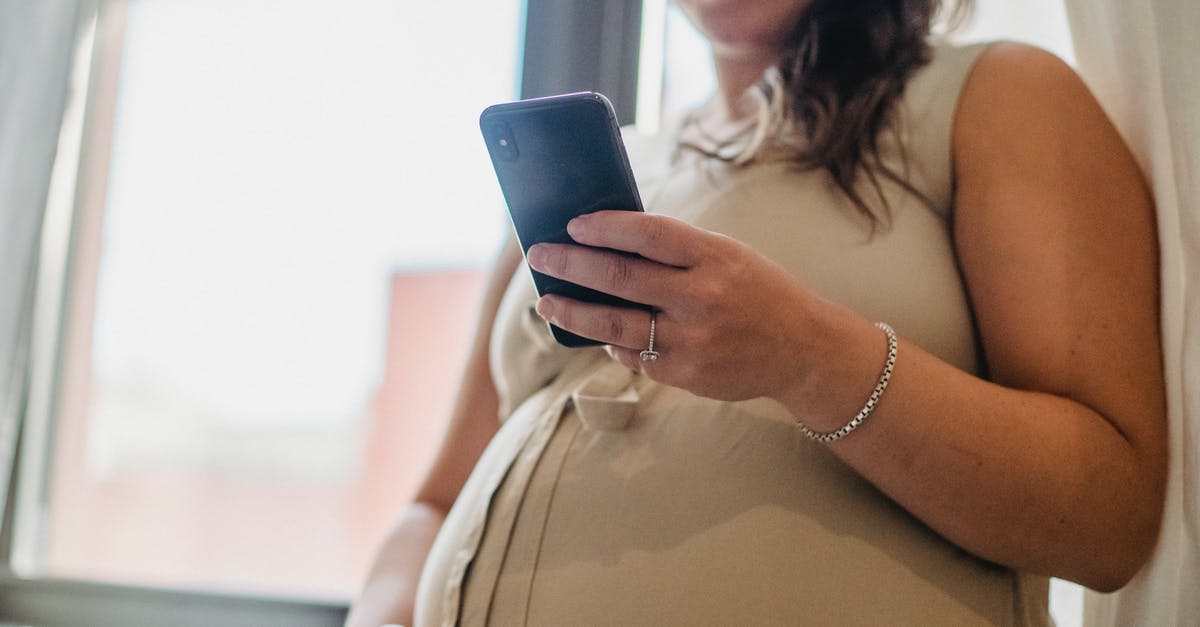 Any idea of wait times for a visa from US? - From below of unrecognizable pregnant female standing near window in room with cellphone and checking notifications in daytime