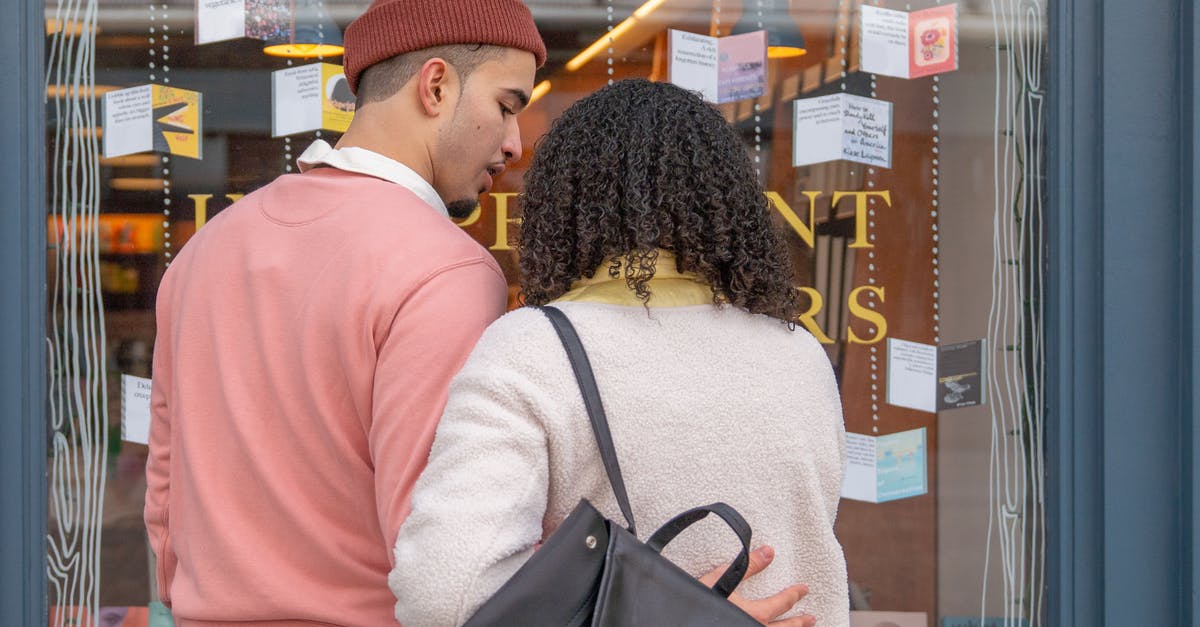 Anyone tried to bond merchandise in Qatar airport? - Back view of young Hispanic couple in stylish clothes cuddling while standing near glass showcase of bookstore during weekend in city