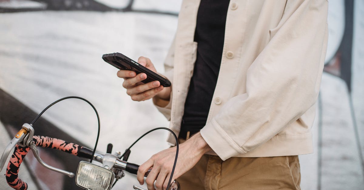 App for bicycle navigation in Prague? - Anonymous man using smartphone while standing on street near bicycle