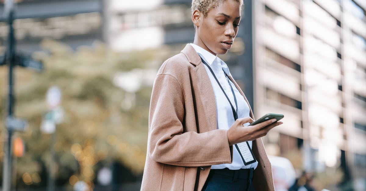 App where one can specify transit city - Focused black businesswoman browsing smartphone on urban street