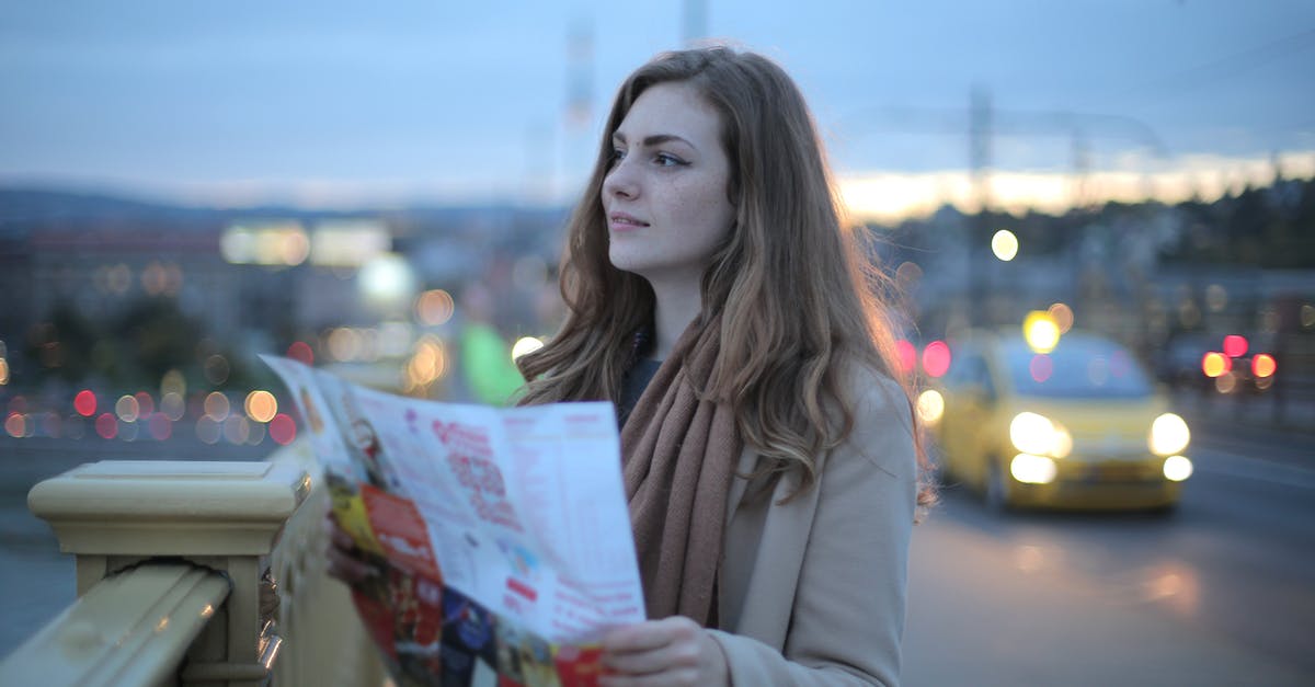 Application to plan optimal route between multiple cities - Female traveler in warm clothes standing on street with map and looking away at dusk