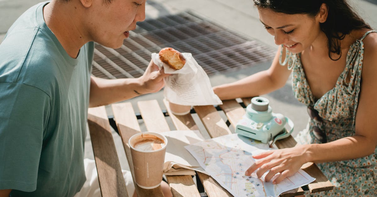 Application to plan optimal route between multiple cities - Diverse couple having breakfast in cafe while exploring map