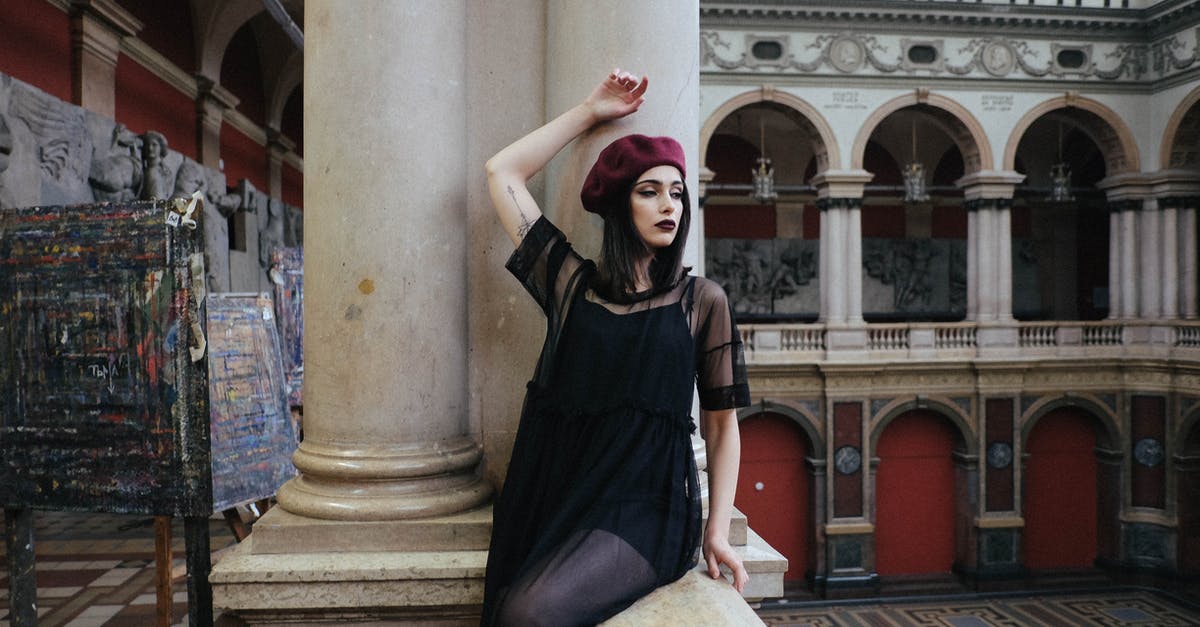 Apply for a Russian visa in English in Strasbourg - Young contemplative tattooed woman in trendy wear with makeup sitting with raised arm on masonry fence near column in building and looking away