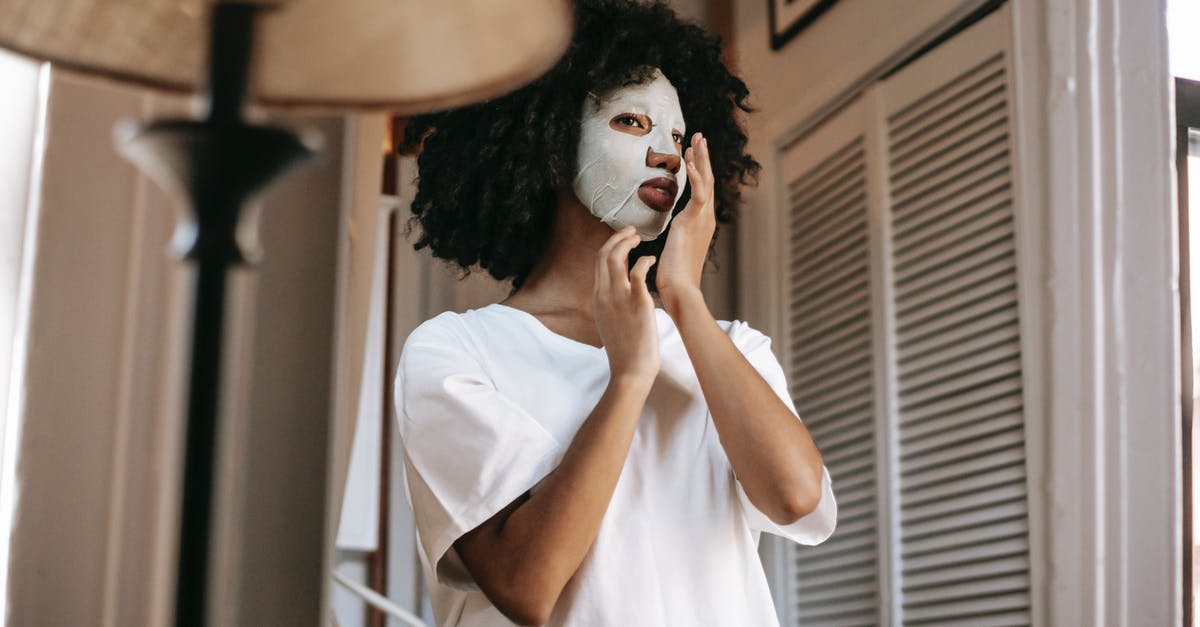 Apply for F1 from home country after B1 extension - From below of African American female with dark curly hair with sheet mask in casual clothes standing in room and touching face in daytime