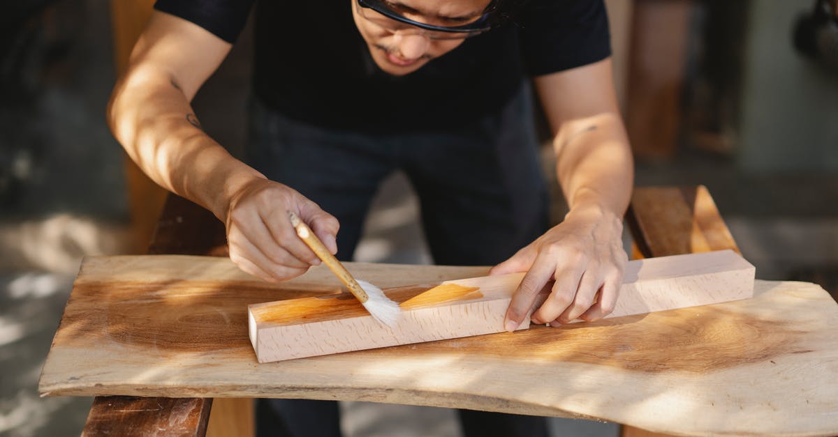 Apply schengen visa multiple entry for several business trips - Young ethnic carpenter applying protective varnish on wooden detail while working in professional workshop