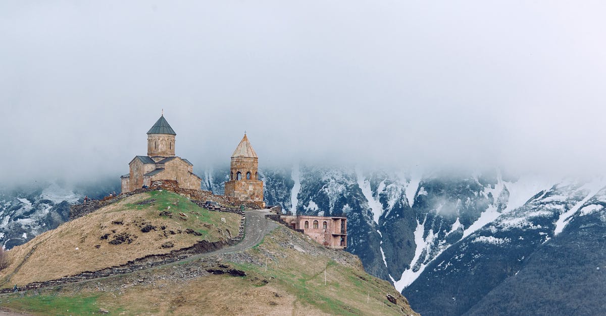 Applying for a Georgia tourism visa - Medieval church on grassy hilltop surrounded by majestic mountains