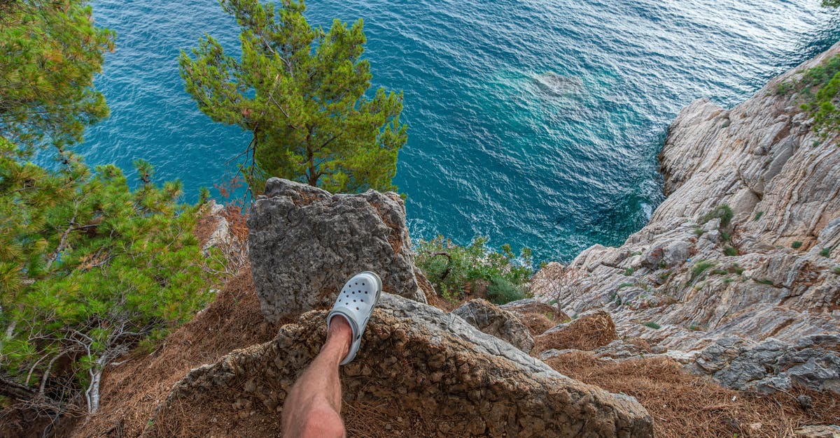 Applying for a visa from outside country of origin - From above of anonymous male traveler standing on edge of rocky cliff above above azure rippling sea in tropical country