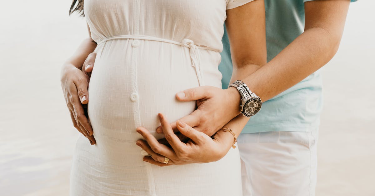 Applying for belgium visa with pregnant wife [closed] - Crop anonymous young man in casual clothes embracing belly of pregnant wife while standing on seashore