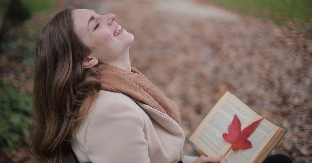 Appropriate clothing for Pantanal in Brasil during the dry season - Cheerful young woman with red leaf enjoying life and weather while reading book in autumn park